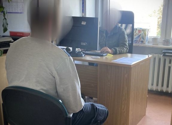 policjant siedzi za biurkiem na przeciwko niego siedzi zatrzymany mężczyzna