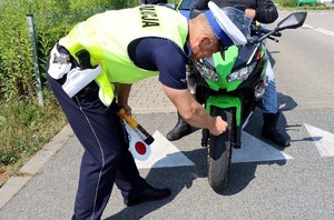 Umundurowany policjant kontroluje oponę w motocyklu.