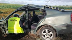 Zdjęcie przedstawia klęczącego umundurowanego policjanta przed rozbitym autem.